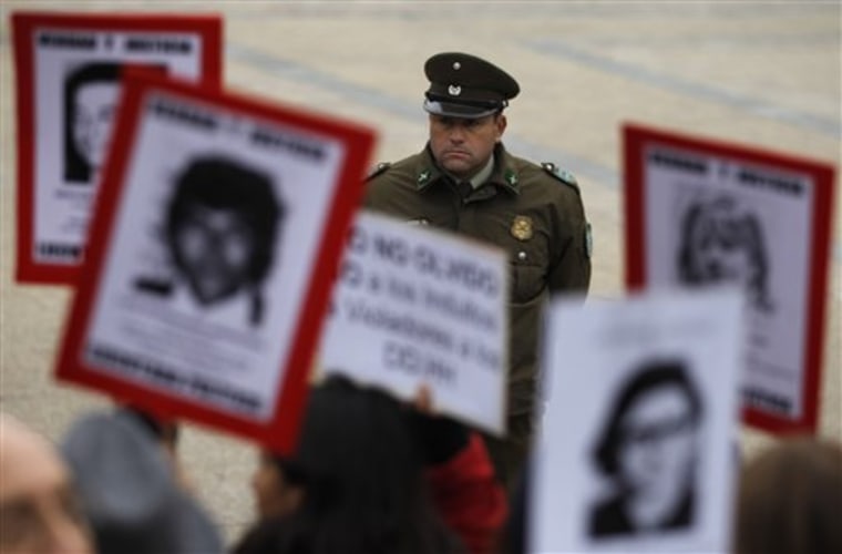 A police officer looks on Wednesday as people hold portraits of family members who were dissidents killed during the dictatorship of former Gen. Augusto Pinochet. They are demonstrting outside La Moneda government palace in Santiago, Chile. The Roman Catholic Church handed Chile's President Sebastian Pinera a petition for massive pardons that include military officials who committed crimes against humanity during Pinochet's dictatorship.
